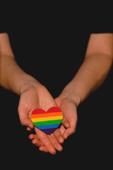 Female arms holding the heart coloured in LGBT pride colours on the dark background. Concept of the International Day Against Homophobia concept, sexual equality, feminism, social safety