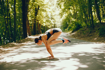 Pretty lady training in a summer park. Brunette doing yoga. Girl in a black top