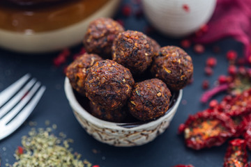 Bowl of raw vegan meat balls surrounded with vegetables on a dark tabletop flat lay. Veggie meatballs. 