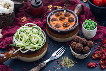Bowl of raw vegan meat balls surrounded with peas and zucchini noodles and vegetables on a dark tabletop flat lay. Veggie meatballs.