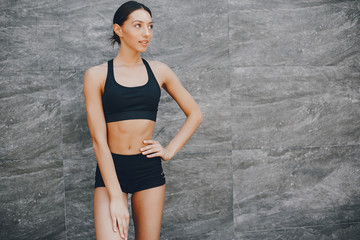 Pretty lady standing in a summer city. Brunette in a black top. Woman near gray wall
