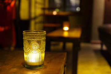 Burning candle in translucent craft glass jar with pattern on wooden bar table