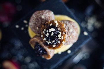 Vegan cashew dumplings with plum jam on a dark tabletop. Crumbs of dehydrated almond and coconut sugar. Flat lay with healthy vegan sweet balls 
