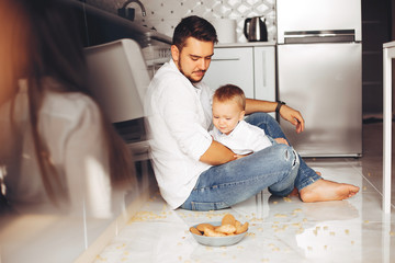 Little boy sitting on a floor. Handsome father in a white shirt. Family in a kitchen