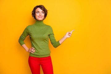 Photo of pretty lady indicating finger looking empty space advising black friday low prices wear casual green turtleneck red trousers isolated yellow color background