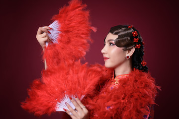 Beautiful asian woman wearing red traditional vintage chinese dress holding feather fan on red background, Thailand