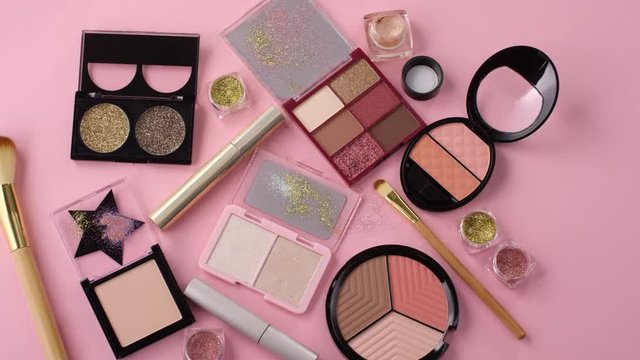 Top view shot of set of decorative cosmetics products on table. There are eyeshadows, glitter, powder, face palette, mascara and brushes