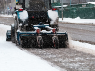 Tractor cleaning sidewalk from snow with snow plow and rotating brush.