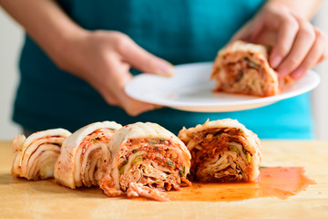 Kimchi cabbage on wooden board and hand holding kimchi on plate, Korean food
