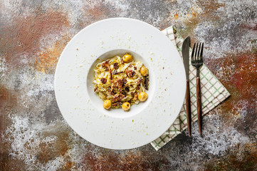 Fettuccini pasta with chanterelle mushrooms, olives and pesto in a white plate. Italian Mediterranean cuisine. Top view
