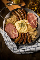 Sauerkraut Pfanne mit Nürnberger Rostbratwürste, Kassler Nacken,  Kartoffelpüree Senf und Bier auf Holz Tisch