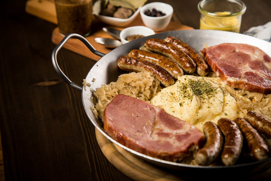 Sauerkraut Pfanne mit Nürnberger Rostbratwürste, Kassler Nacken,  Kartoffelpüree und Senf auf Holz Tisch