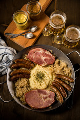 Sauerkraut Pfanne mit Nürnberger Rostbratwürste, Kassler Nacken,  Kartoffelpüree Senf und Bier auf Holz Tisch