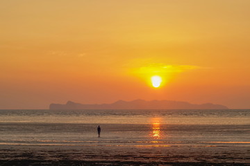 view seaside evening of a man walking on sand beach with sundown and orange sun light in the sky background, sunset at Chao Mai Beach, Chao Mai National Park, Trang Province, southern of Thailand.