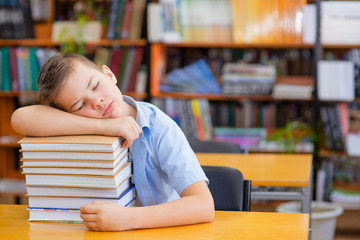 Cute boy in the library lies and sleeps on a stack of books