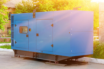 Diesel generator for emergency power supply at the wall of a medical center against the backdrop of green trees in fine sunny weather. - obrazy, fototapety, plakaty