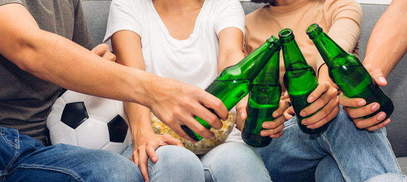 Group of friends eating popcorn and drinking beer together and watching soccer game on sofa at home.Friendship and party concept