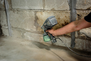 Worker applying primer on prepped wall, using spray gun.