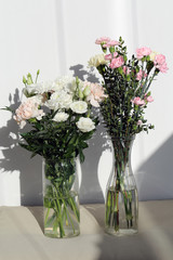 Super cute, light color flower bouquets including baby pink and white dianthus flowers with white chrysanthemum flowers, and some other white flowers. Photographed with a white wall on the background.