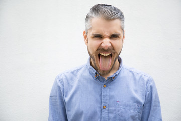 Handsome bearded man showing tongue. Front view of careless young guy posing. Teasing concept