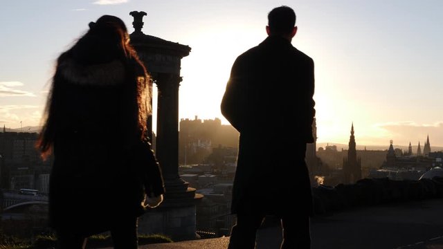 View from Calton Hill in Edinburgh, Scotland at Sunset. View or cityscape skyline with Castle in the distance. Tourists walk past