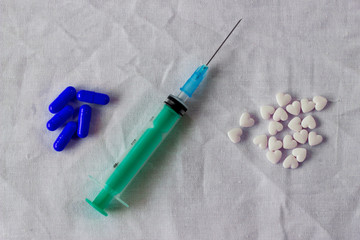 Blue pills, syringe and white pills in the shape of a heart on a white crumpled hospital tissue. The concept of illness and recovery, coronavirus, life after illness, flu, virus, mine space.