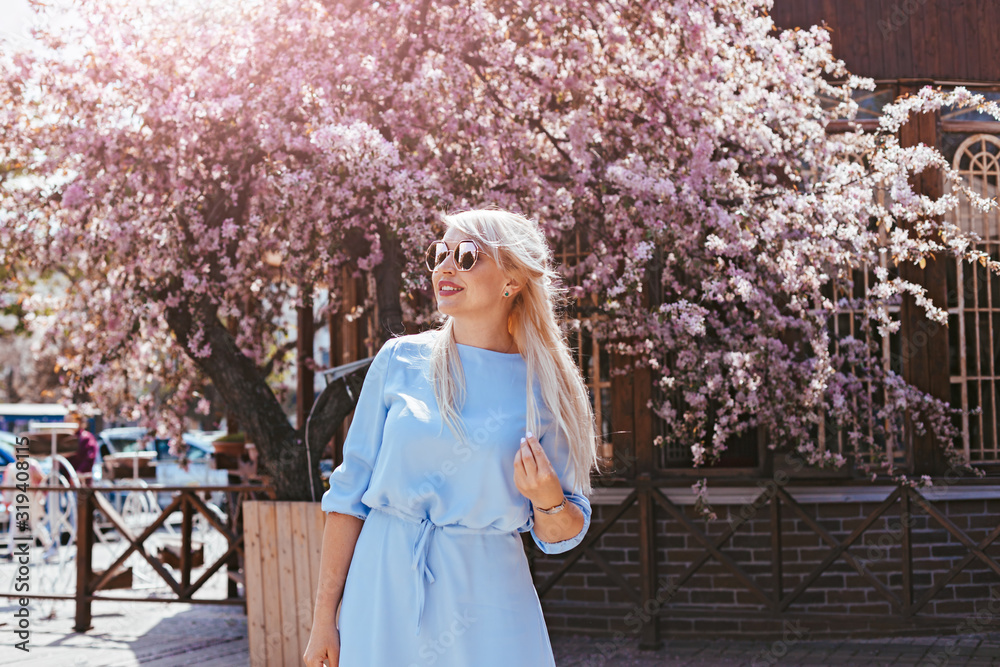 Wall mural Beautiful model in blue dress by spring blooming tree