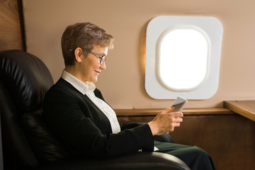 beautiful aged woman in the cabin of a private plane in a chair with a tablet in her hands