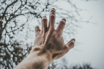 male left hand reaching for dark blue sky with copy space for text. point view shot of human hand. Color toned image. Concept of religion, freedom, help,dream.