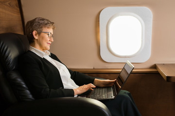 beautiful aged woman in the cabin of a private plane in a chair with a laptop
