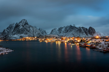 Winter panorama of Reine village at night and outstanding snowy mountains on horizon. Lofoten islands, Norway. © juhrozian