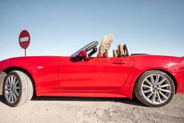 Woman traveling on converrtible sports car, pulling legs out the window. Side view on the red car...