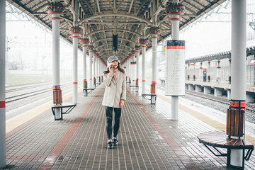 Young woman in winter coat and hats talking on phone and waiting on railway station for train. A girl is wating a train in a trian station at Europe.