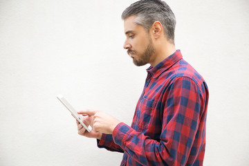 Thoughtful young man using tablet. Side view of guy holding tablet in hands. Technology and communication concept