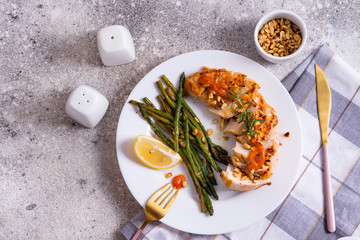 Grilled chicken breast with grilled asparagus and lemon slice on dark stone background . Paleo diet.