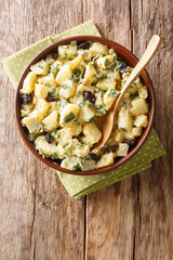 African potato salad with yogurt, herbs, spices and dried olives close-up in a bowl. Vertical top view