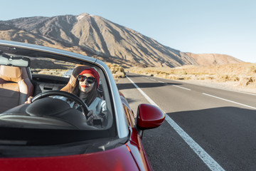 Young woman traveling by convertible car on the picturesquare desert valley, sitting at the driver seat. Front view through windshield