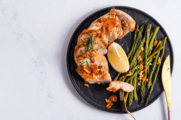 Grilled chicken breast with grilled asparagus and lemon slice on stone background . Paleo diet.