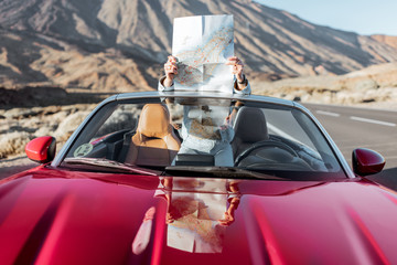 Fototapeta na wymiar Woman sitting with map on the convertible car, enjoying road trip on the desert valley with volcano on the background