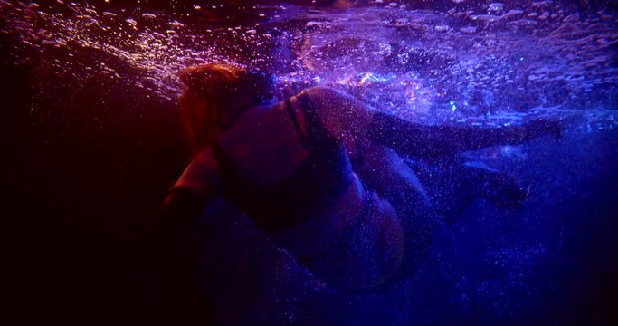 woman fall in swimming pool in night club, underwater shot of plunge