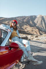 Young woman enjoying road trip on the desert valley, sitting on the convertible car on the roadside with volcano on the background