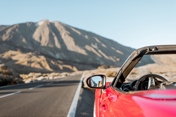 Convertible car on the roadside of the desert valley with volcano on the background, traveling by...