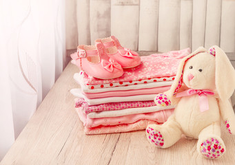Baby clothes and baby shoes for a newborn girl in pink with a plush bunny.