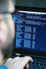 Hacker in glasses breaking code. Criminal hacker penetrating network system from his dark hacker...