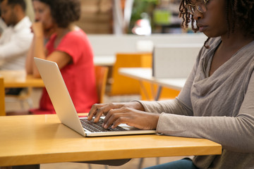 Cropped shot of thoughtful woman working with laptop at library. Concentrated African American woman typing on laptop. Technology concept