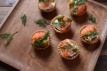 Tartalets with fresh salmon, philadelphia cream cheese, olives on wooden background