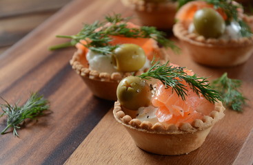 Tartalets with fresh salmon, philadelphia cream cheese, olives on wooden background