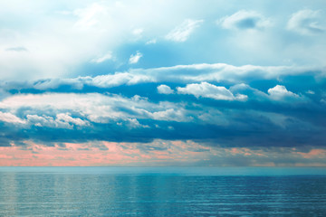 Naklejka na ściany i meble Beautiful dramatic textured cumulus clouds at sunrise over a calm sea