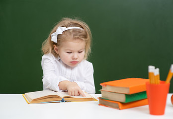 Girl at school in the classroom, sitting on the background of a green blackboard and reading a book