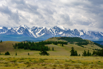 Panoramic view of the North-Chui mountain range under cloudy sky. Kurai steppe and snow-capped peaks of Altai mountains.